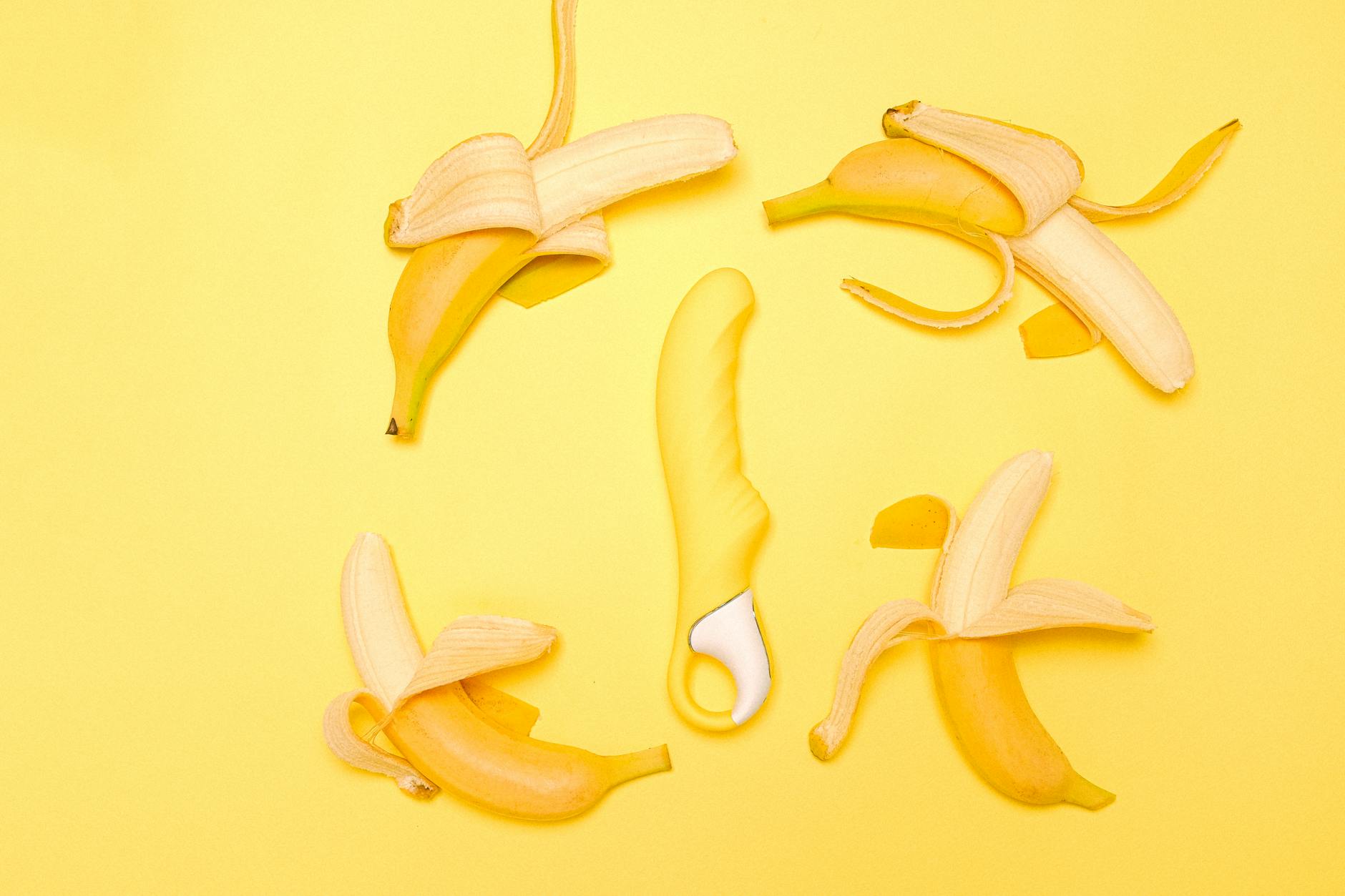A creative flat lay of a yellow silicone lemon vibrator surrounded by fresh lemons on a bright yellow background.