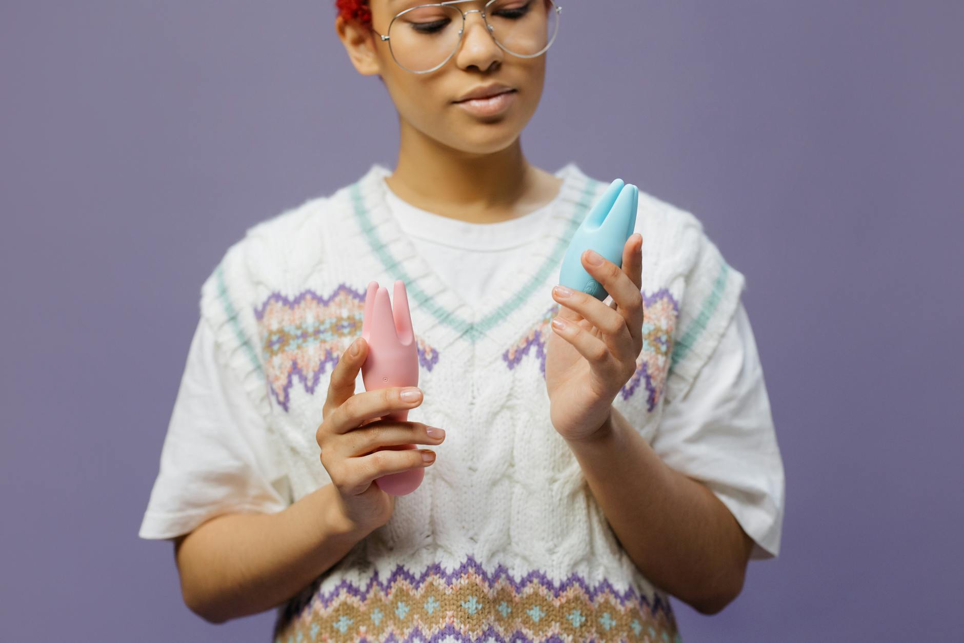 Woman holding blue and pink silicone vibrators in thoughtful pose